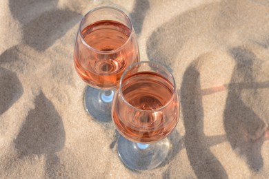 Glasses of tasty rose wine on sand, closeup
