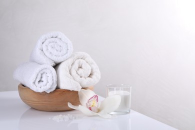 Spa composition with towels, orchid flower, candle and sea salt on white table, space for text