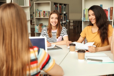 Photo of Young people discussing group project at table in library