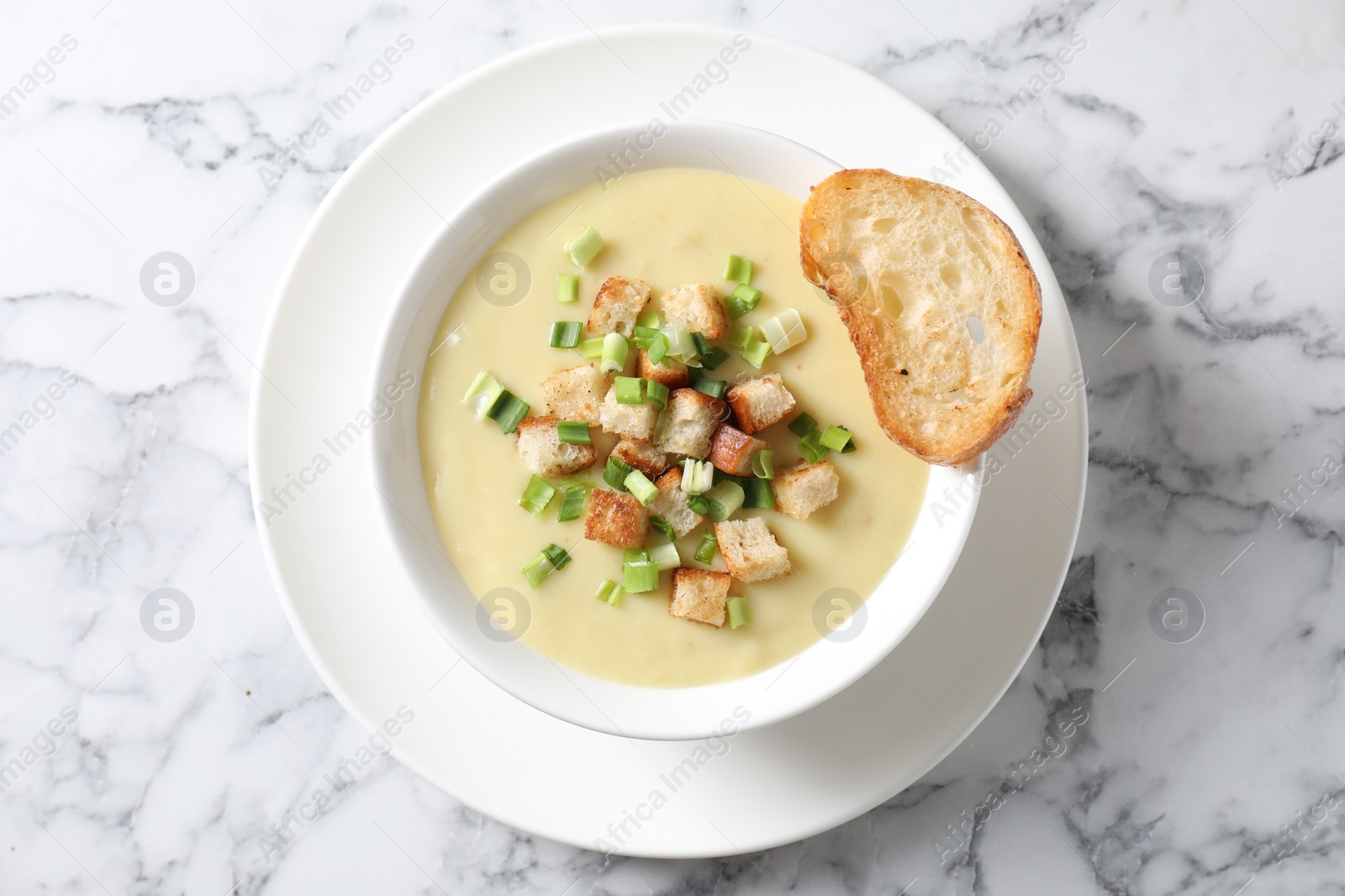 Photo of Tasty potato soup with croutons and green onion in bowl on white marble table, top view