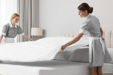 Professional chambermaids making bed in hotel room