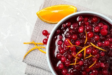 Photo of Fresh cranberry sauce and slice of orange on light marble table, flat lay