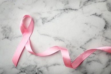 Photo of Pink ribbon on marble background, top view with space for text. Breast cancer awareness concept