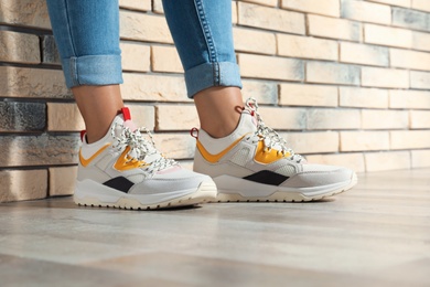 Woman in stylish sneakers near brick wall indoors, closeup