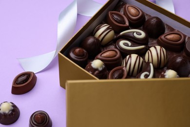 Open box of delicious chocolate candies on violet background