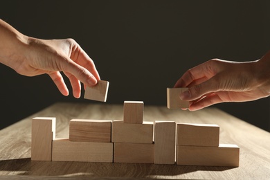 Photo of People constructing with wooden building blocks, closeup. Corporate social responsibility concept