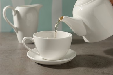 Pouring aromatic tea in cup at gray table, closeup