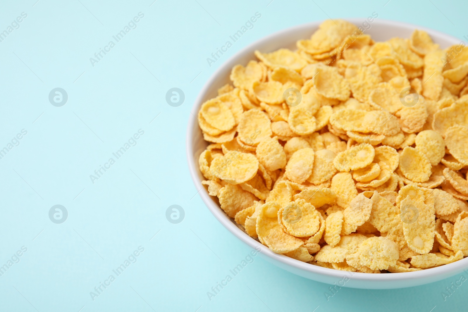 Photo of Breakfast cereal. Tasty corn flakes in bowl on light blue table, closeup. Space for text