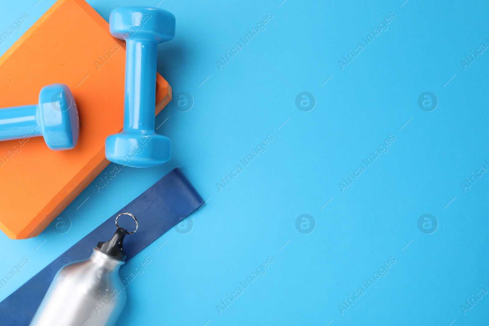 Photo of Two dumbbells, yoga block, fitness elastic band and thermo bottle on light blue background, flat lay. Space for text