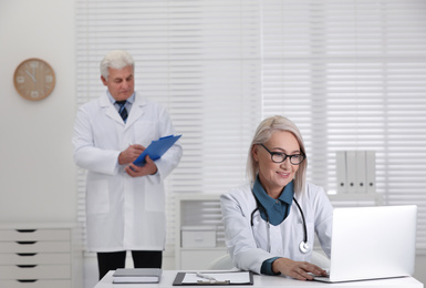 Mature female doctor working with laptop at table in office