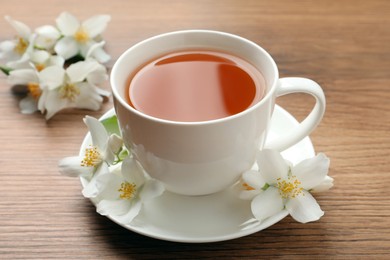Photo of Cup of aromatic jasmine tea and fresh flowers on wooden table