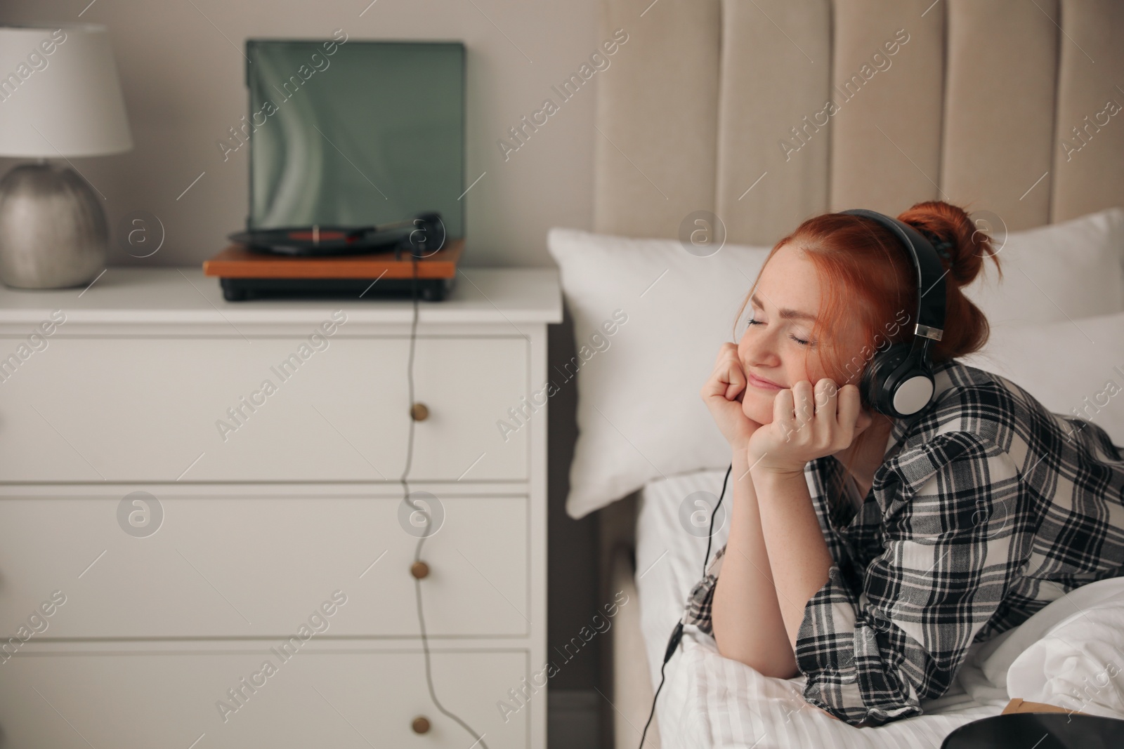 Photo of Young woman listening to music with turntable in bedroom
