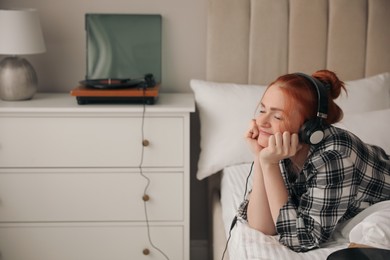 Young woman listening to music with turntable in bedroom