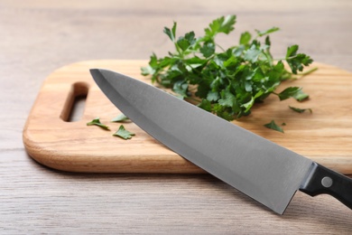 Cutting board with chef's knife and fresh parsley on wooden table