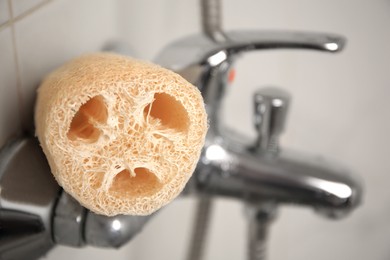 Photo of Natural loofah sponge on faucet in bathroom, closeup