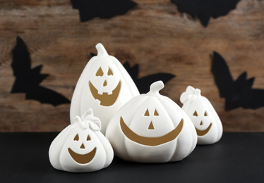 White pumpkin shaped candle holders on black table against wooden wall with paper bats. Halloween decoration