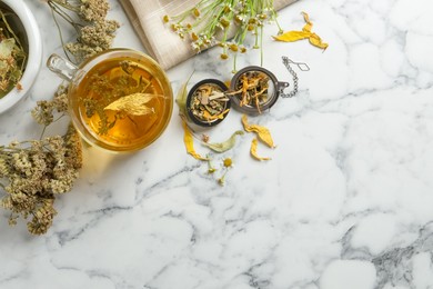 Photo of Freshly brewed tea and dried herbs on white marble table, flat lay. Space for text