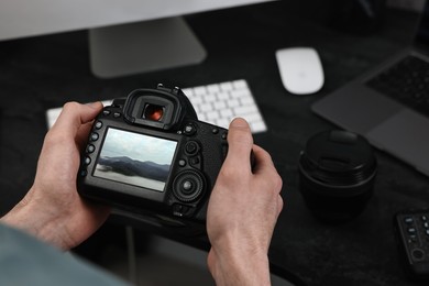 Man with professional photo camera looking at shot of mountain indoors, closeup