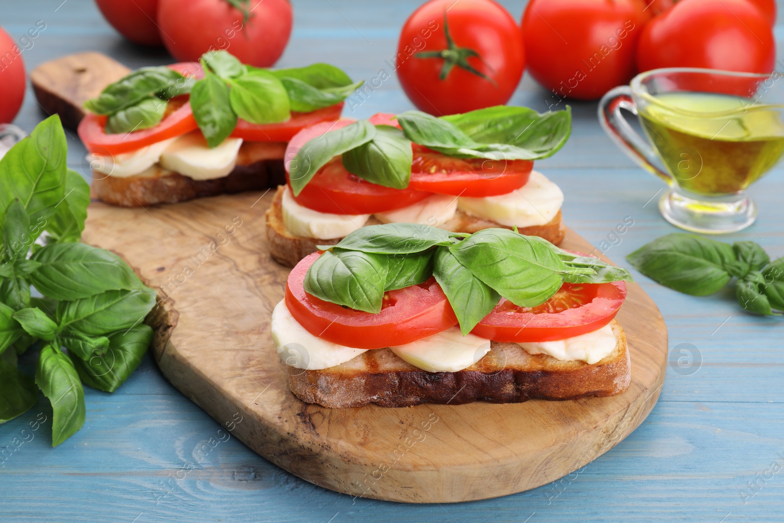 Photo of Delicious Caprese sandwiches with mozzarella, tomatoes and basil on light blue wooden table