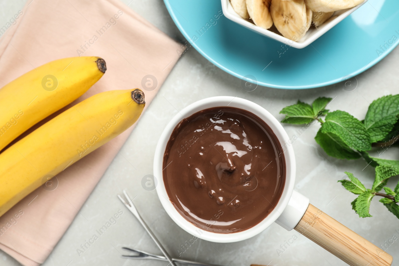 Photo of Fondue pot with milk chocolate and bananas on light table, top view