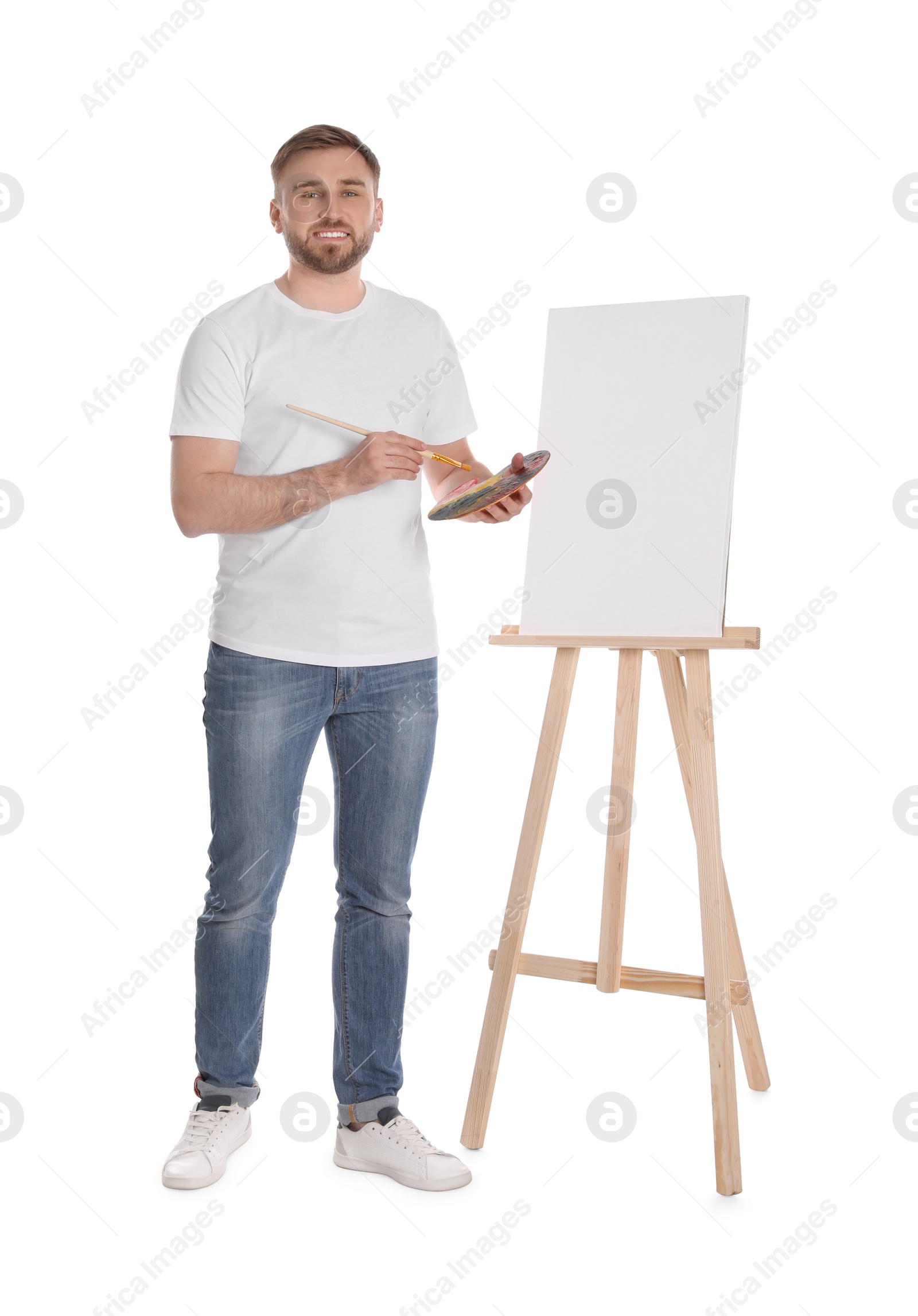 Photo of Man with painting tools near easel on white background. Young artist