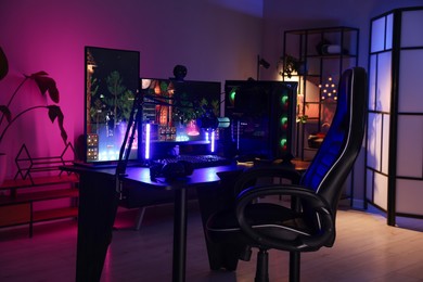 Photo of Playing video games. Stylish room interior with modern computer and gaming chair in neon lights