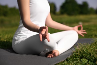 Woman practicing yoga on mat outdoors, closeup. Lotus pose