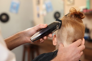 Photo of Professional hairdresser cutting boy's hair in beauty salon, closeup