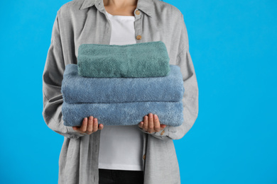 Photo of Woman holding fresh towels on light blue background, closeup