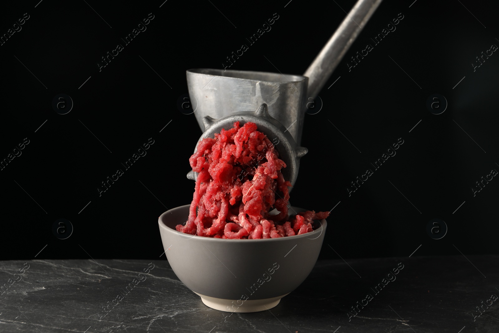 Photo of Metal meat grinder with beef mince on dark textured table against black background