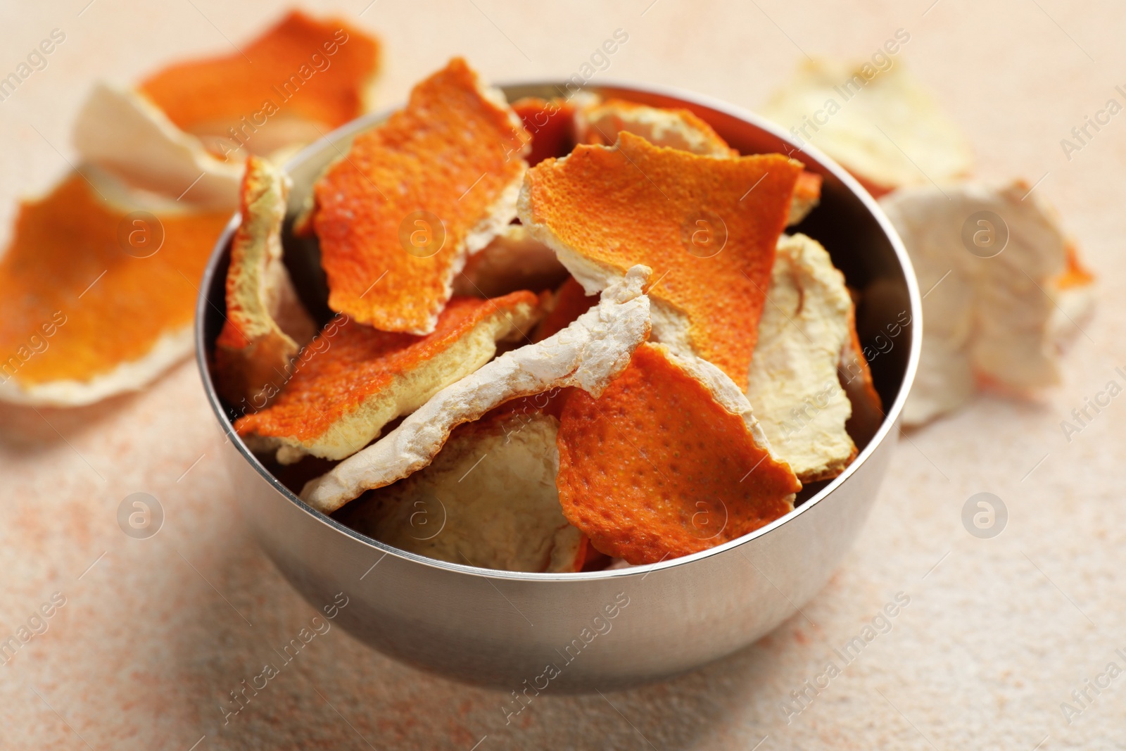 Photo of Dry orange peels in bowl on beige table, closeup