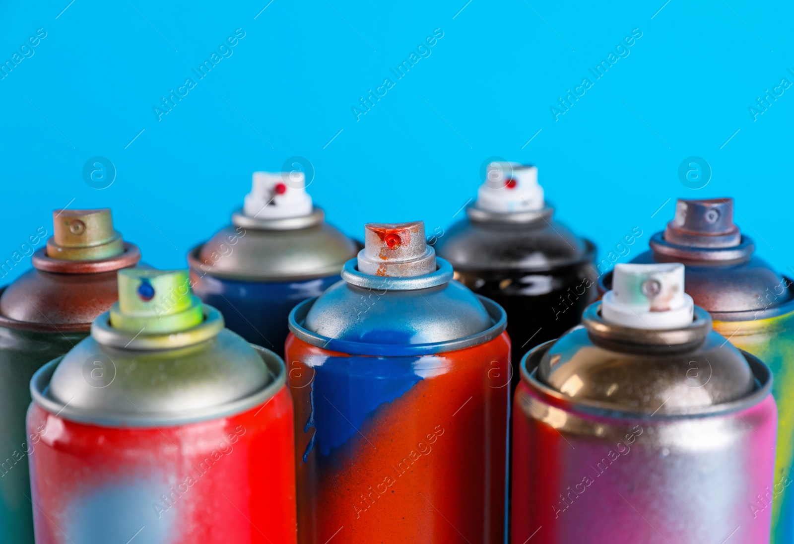 Photo of Used cans of spray paints on light blue background, closeup