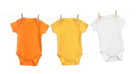 Photo of Colorful baby onesies hanging on clothes line against white background. Laundry day