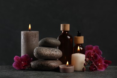 Beautiful composition with burning candles, spa stones and different care products on dark grey table