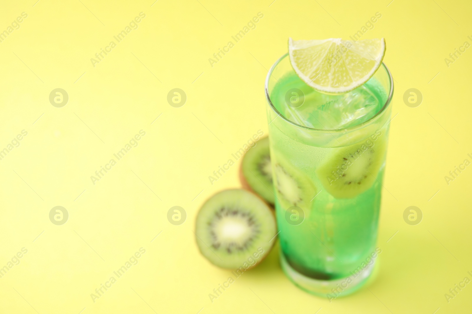 Photo of Glass of refreshing drink and cut kiwi on yellow background, closeup. Space for text