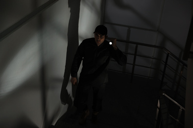 Photo of Male security guard with flashlight going up stairs in darkness
