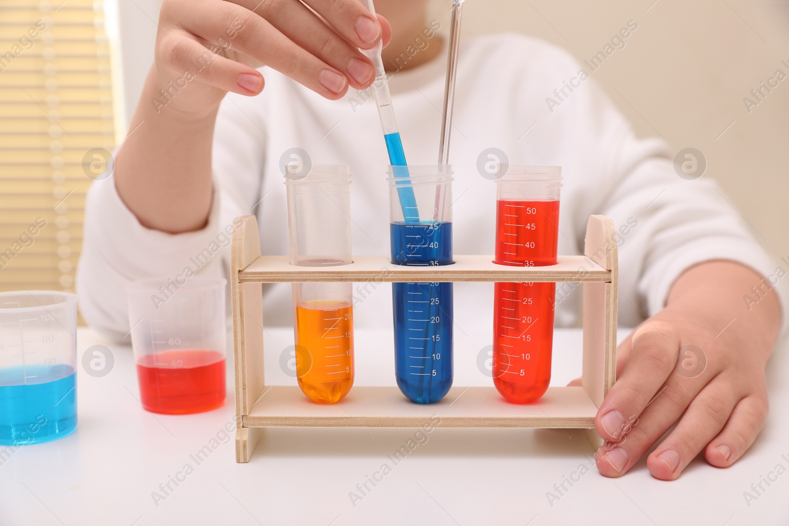 Photo of Girl mixing colorful liquids at white table indoors, closeup. Chemical experiment set for kids