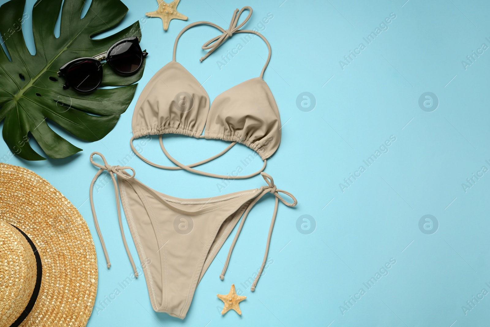 Photo of Stylish beige bikini and beach accessories on light blue background, flat lay. Space for text