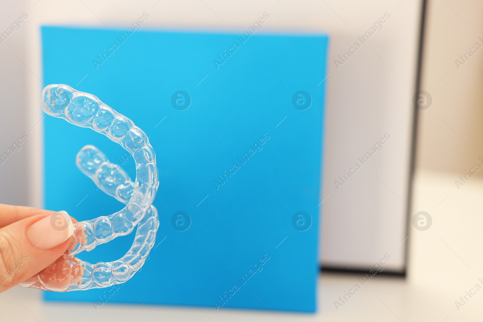 Photo of Woman with transparent dental aligners on blurred background, closeup. Space for text