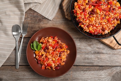 Dish and plate with chili con carne on wooden background, top view