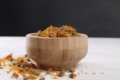 Photo of Bowl with dry calendula flowers on white wooden table, closeup