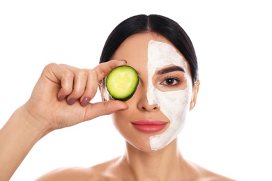 Photo of Young woman with cleansing mask applied on half of face holding cucumber against white background