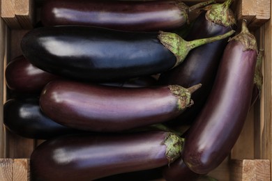 Photo of Ripe eggplants in wooden crate, top view