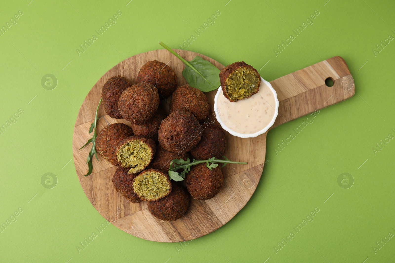 Photo of Delicious falafel balls, herbs and sauce on green background, top view