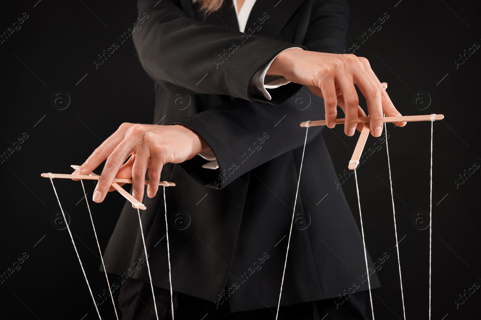 Photo of Woman in suit pulling strings of puppet on black background, closeup