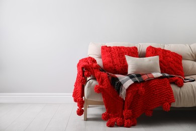 Photo of Sofa with soft pillows and warm plaids near light wall indoors. Space for text