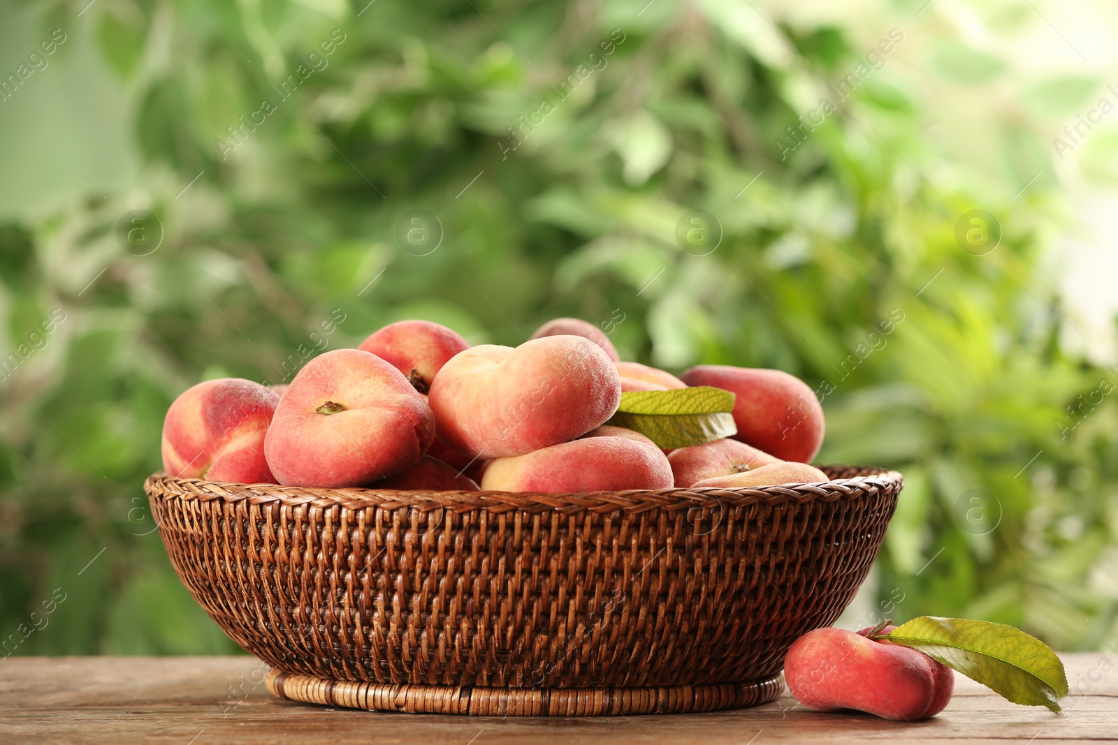 Photo of Fresh ripe donut peaches on wooden table against blurred green background