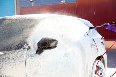 Photo of Worker cleaning automobile with high pressure water jet at car wash