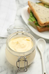 Photo of Jar of delicious mayonnaise near fresh sandwiches on white marble table