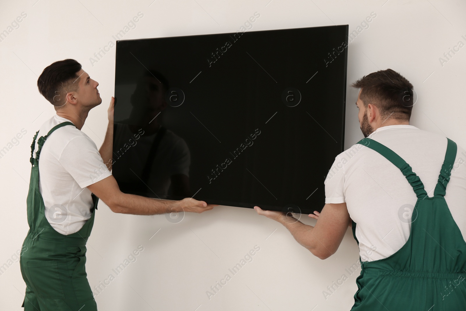 Photo of Professional technicians installing modern flat screen TV on wall indoors